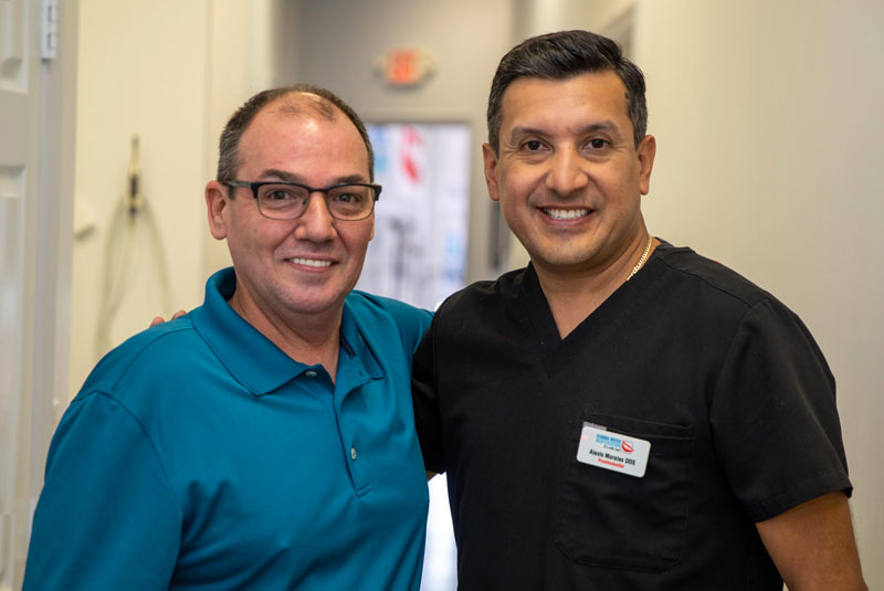 Dr. Alexis Morales With Woody, A Dental Implant Patient, Both Smiling Happily After The Full Mouth Implant Procedure